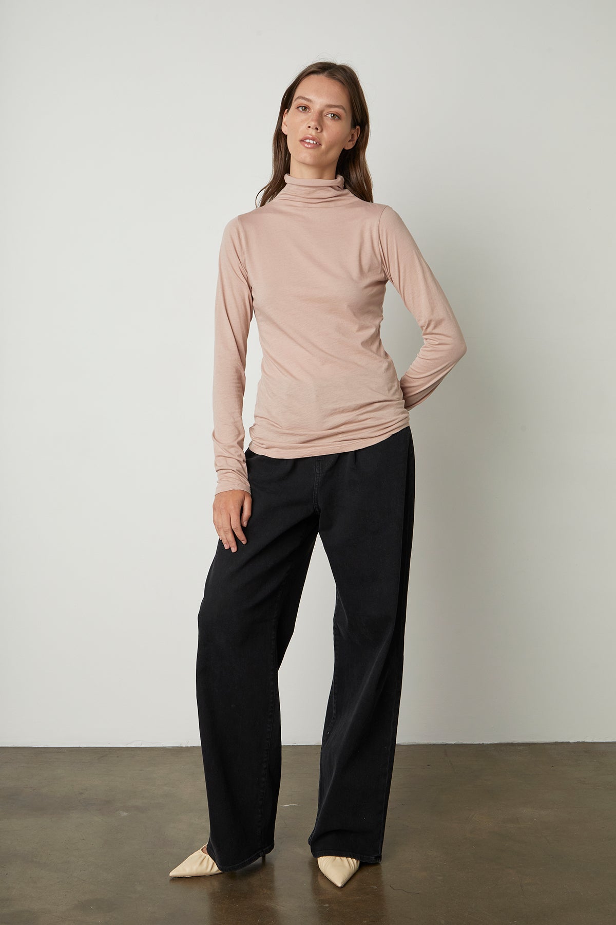   Model standing with arms folded wearing Talisia Gauzy Whisper Fitted Mock Neck Tee in rosegold with harlow denim in noir black with heels full length front 