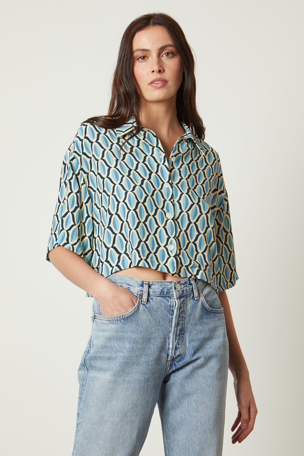 The model is wearing higher waist jeans and a Velvet by Graham & Spencer BECKETT PRINTED BUTTON-UP TOP.-26078942429377