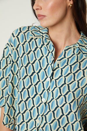 A woman wearing the Velvet by Graham & Spencer BECKETT PRINTED BUTTON-UP TOP, a blue and white patterned shirt.