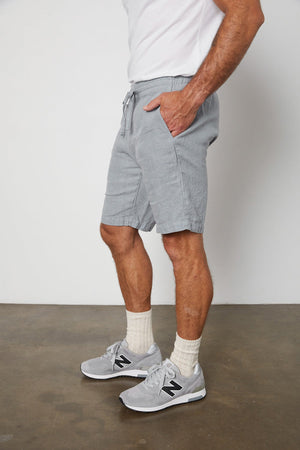 A man wearing JONATHAN LINEN DRAWSTRING SHORT by Velvet by Graham & Spencer and white sneakers.