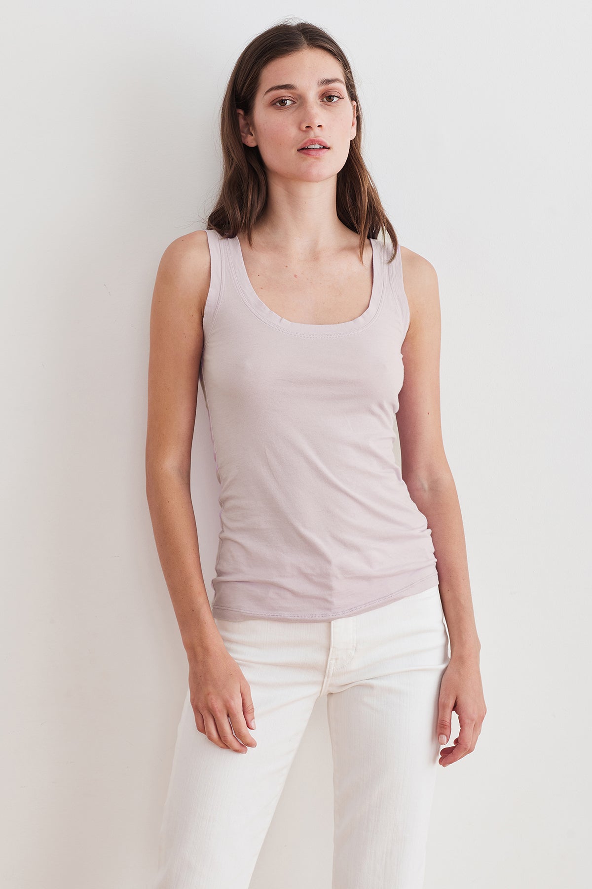   A woman in a Velvet by Graham & Spencer MOSSY GAUZY WHISPER FITTED TANK, paired with white jeans, embracing the back to basics trend in her minimalist outfit. 