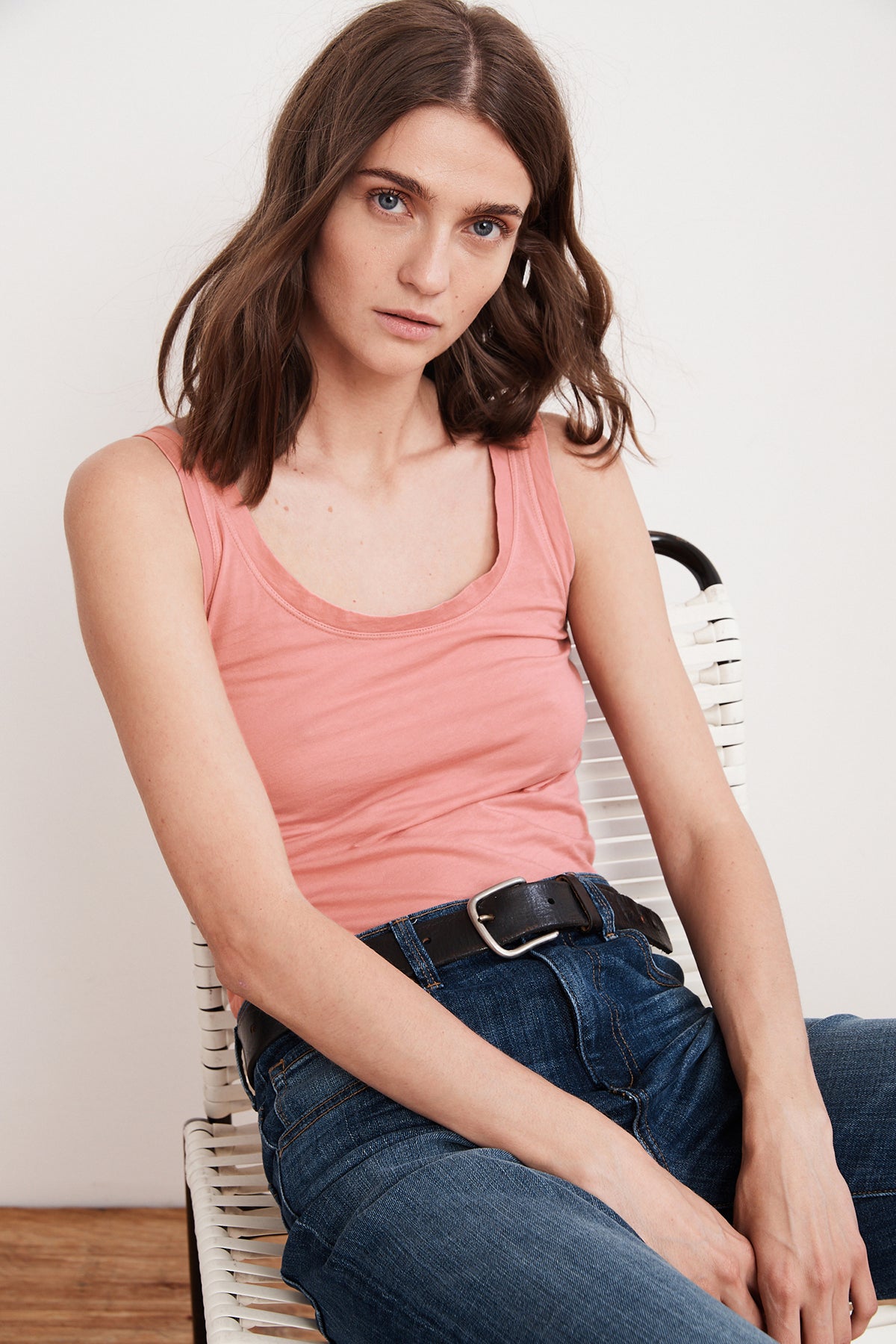   A woman is sitting on a chair wearing jeans and a Velvet by Graham & Spencer MOSSY GAUZY WHISPER FITTED TANK, perfect for warmer days. 