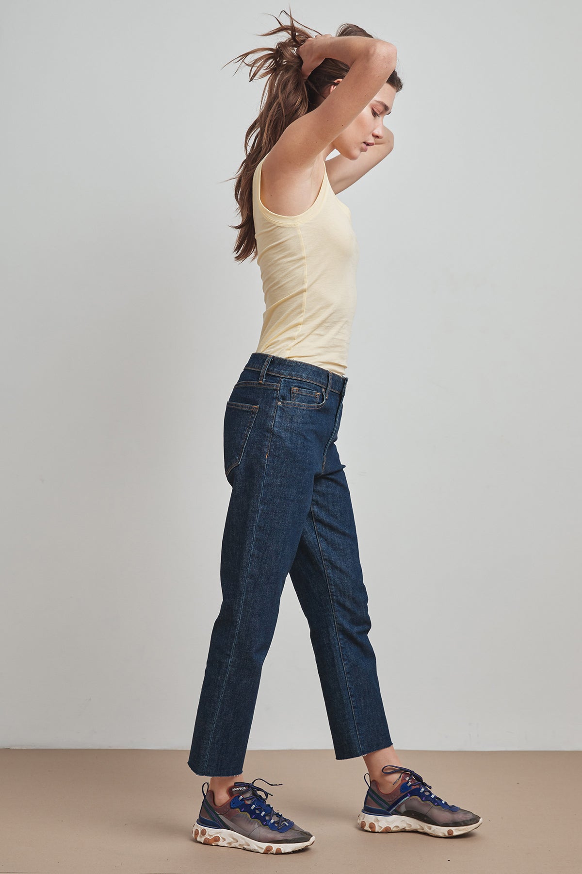   A woman embracing warmer days in a MOSSY GAUZY WHISPER FITTED TANK by Velvet by Graham & Spencer, paired with jeans for a trendy layering option. 