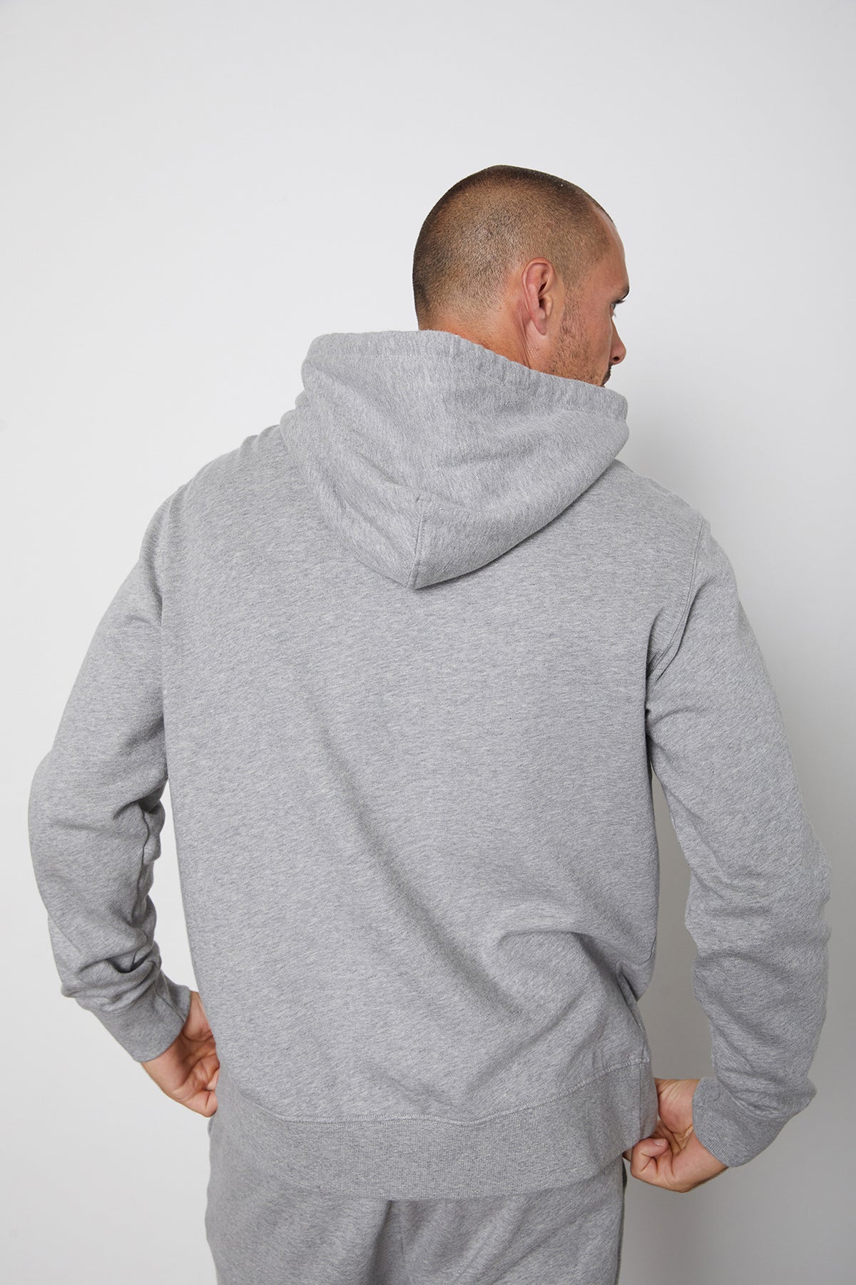 A man is standing with his back to the camera, wearing a Velvet by Graham & Spencer COOPER PULLOVER HOODIE and gray pants.-24522978263233