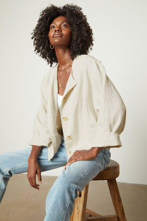 A black woman is sitting on a stool wearing jeans and a Velvet by Graham & Spencer BRIELLE HEAVY LINEN JACKET.