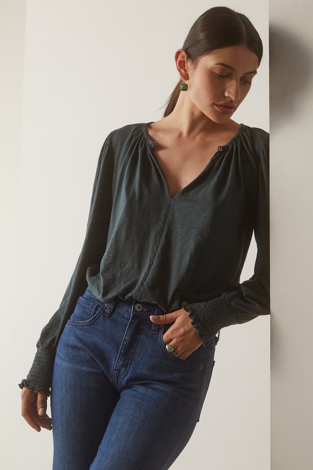   Model Leaning Against a Wall Wearing Irina Split Neck Tee in Bracken front view tucked with denim 