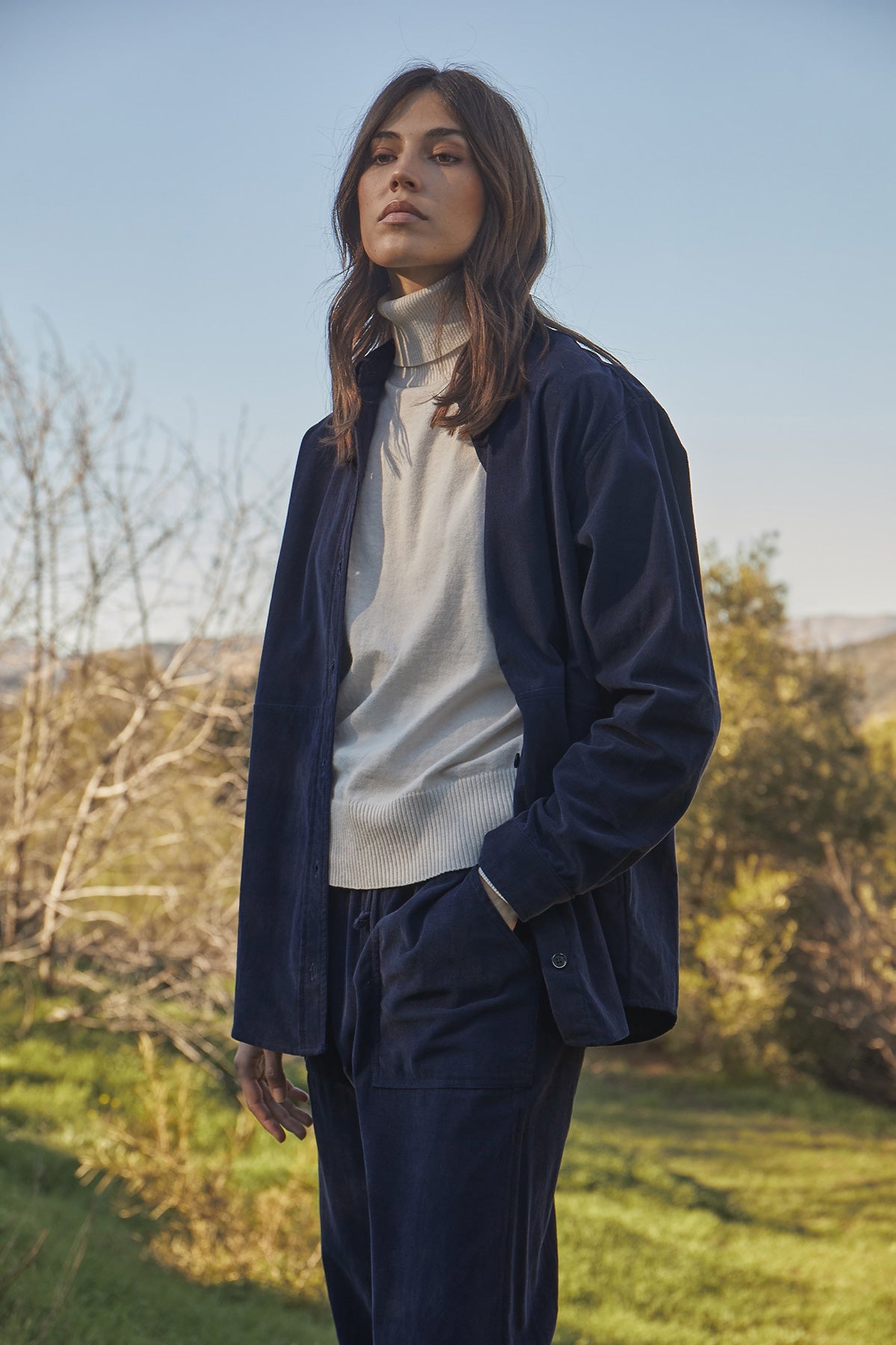   Model standing outside wearing Jeslyn Corduroy Button-Up Shirt in dark blue night color, Renny Sweater and Aspen pants in navy.  