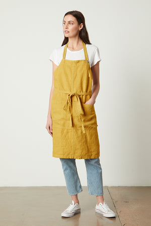 A woman wearing a yellow Jenny Graham Home linen apron made of durable linen with an adjustable neck strap.