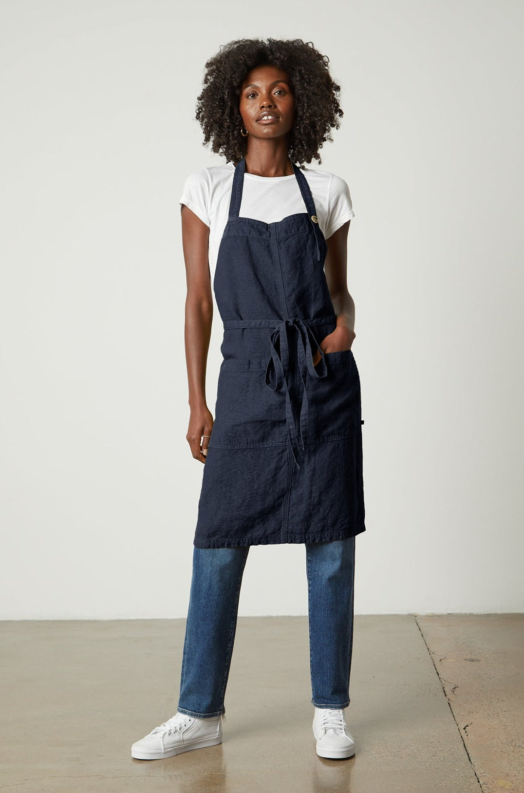   A woman wearing a navy LINEN APRON from Jenny Graham Home and jeans with an adjustable neck strap. 
