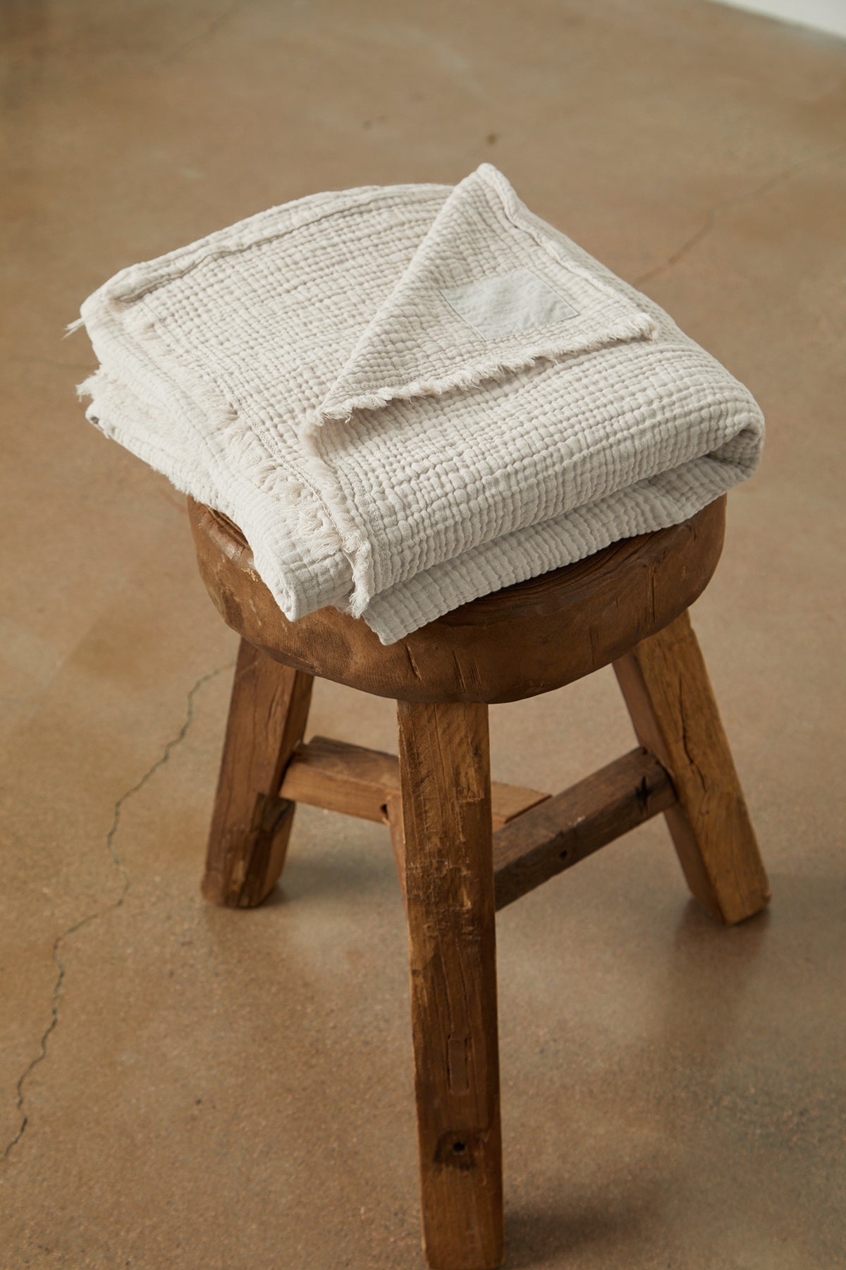   A Jenny Graham Home cotton gauze throw is sitting on a wooden stool. 