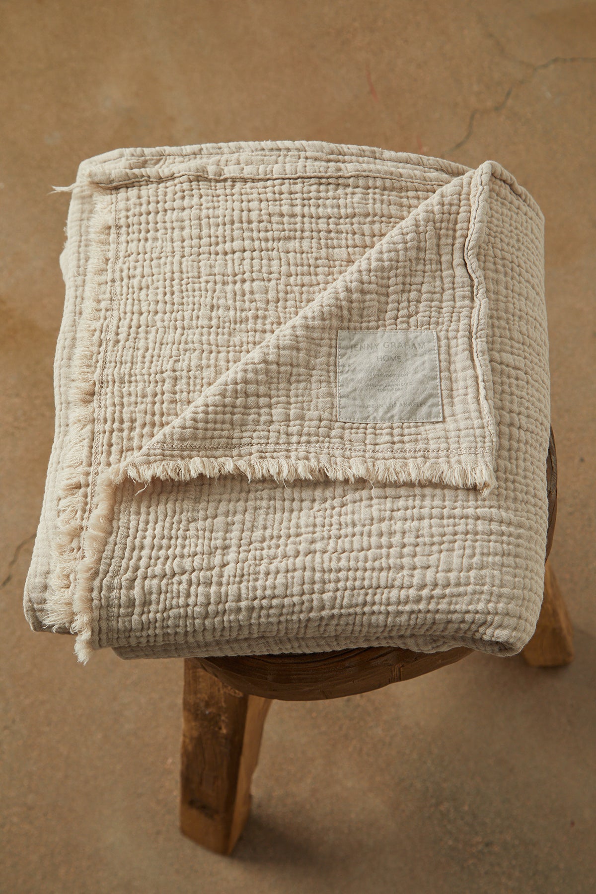   a COTTON GAUZE THROW blanket on top of a wooden stool by Jenny Graham Home. 