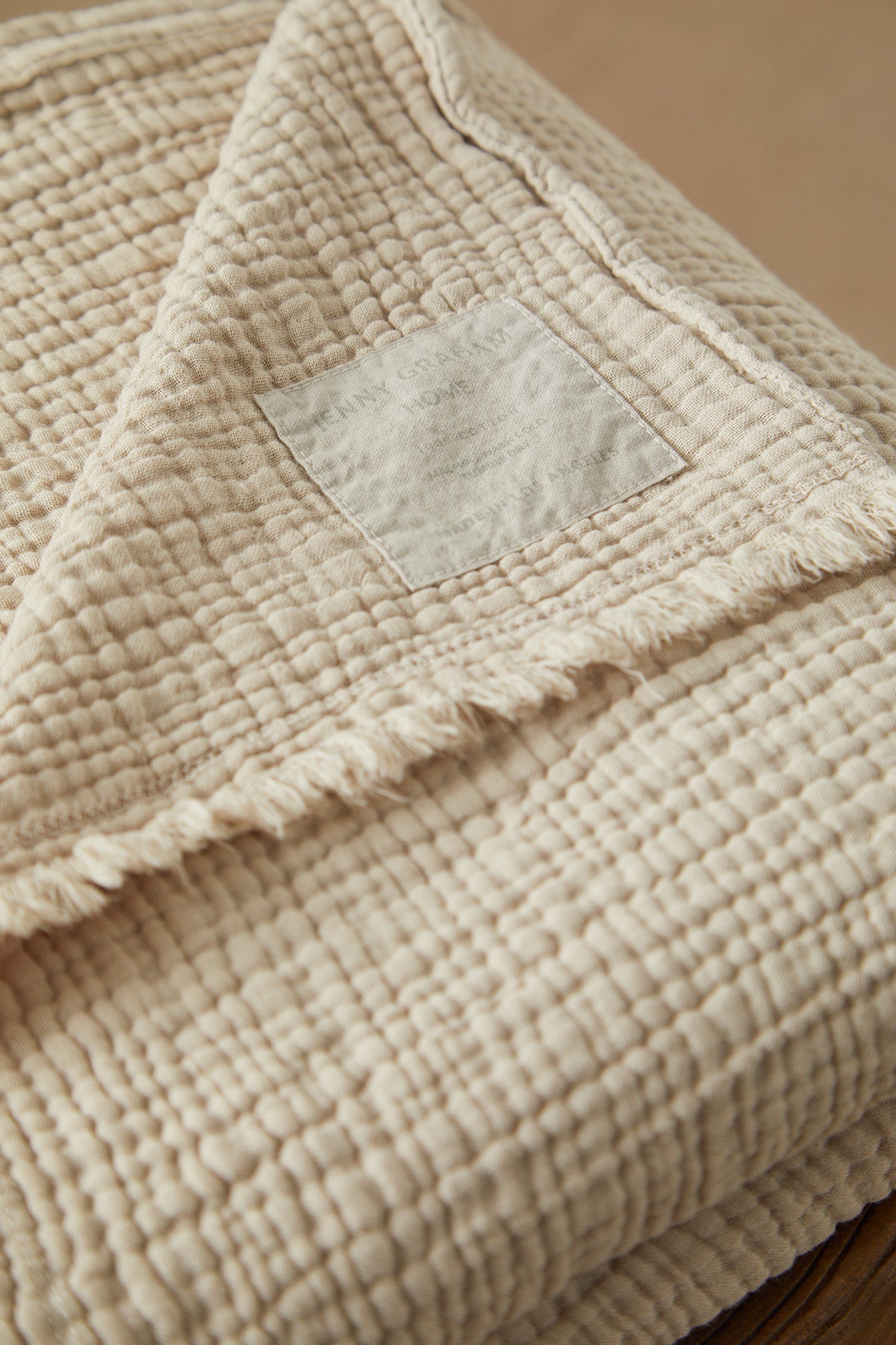   A Jenny Graham Home beige Cotton Gauze Throw folded on top of a wooden table. 
