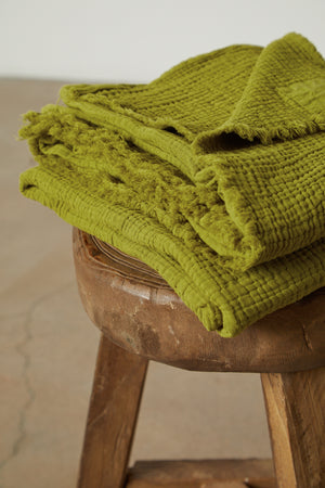 a stack of Jenny Graham Home COTTON GAUZE THROW towels on a wooden stool.