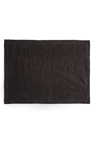 A plain black dyed linen placemat from Jenny Graham Home placed flat on a white background.