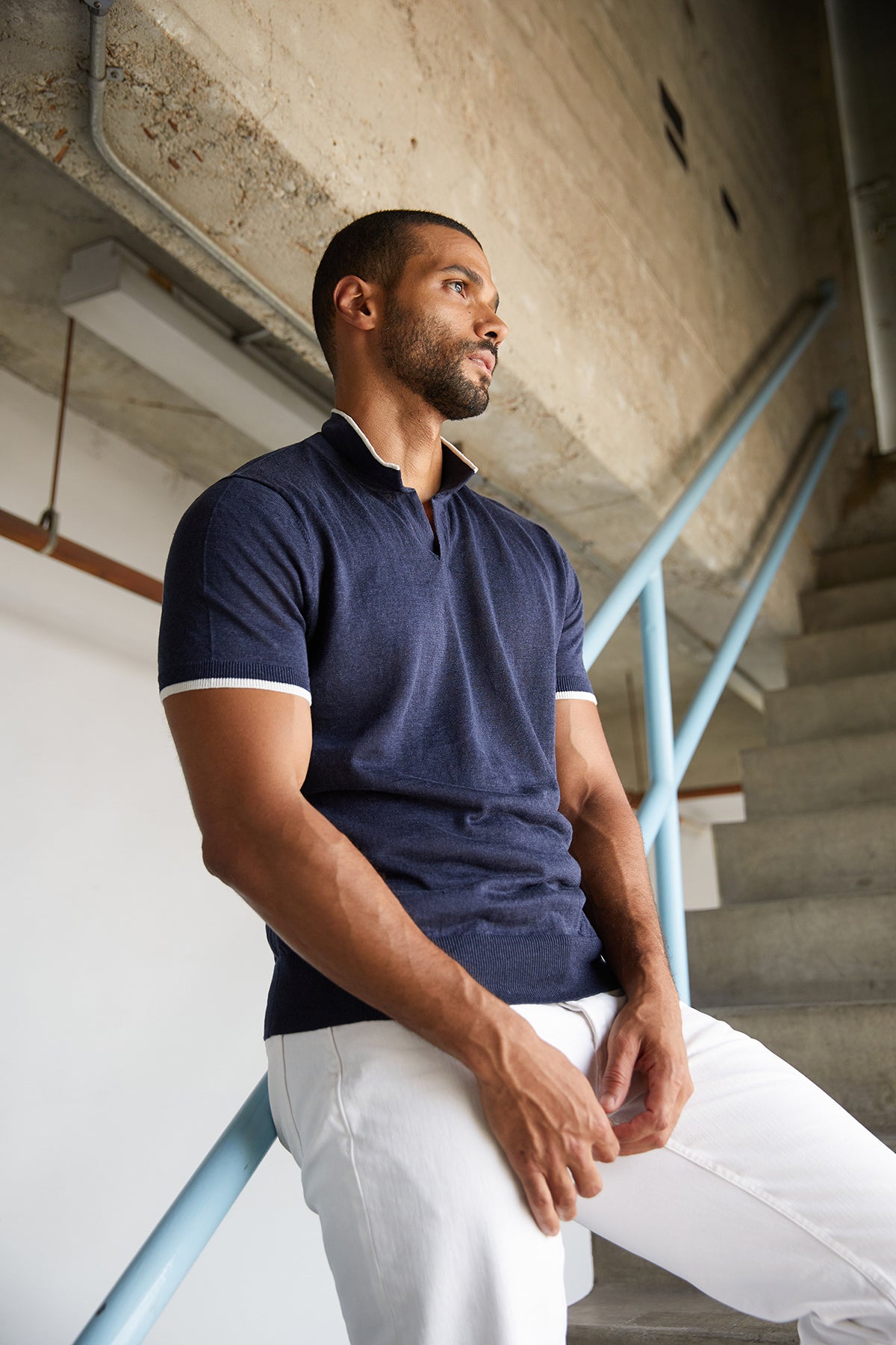 Navy blue Gordon linen blend polo shirt with white stripe trim around sleeves and at collar, with model leaning on stair railing and looking out window-24609082179777