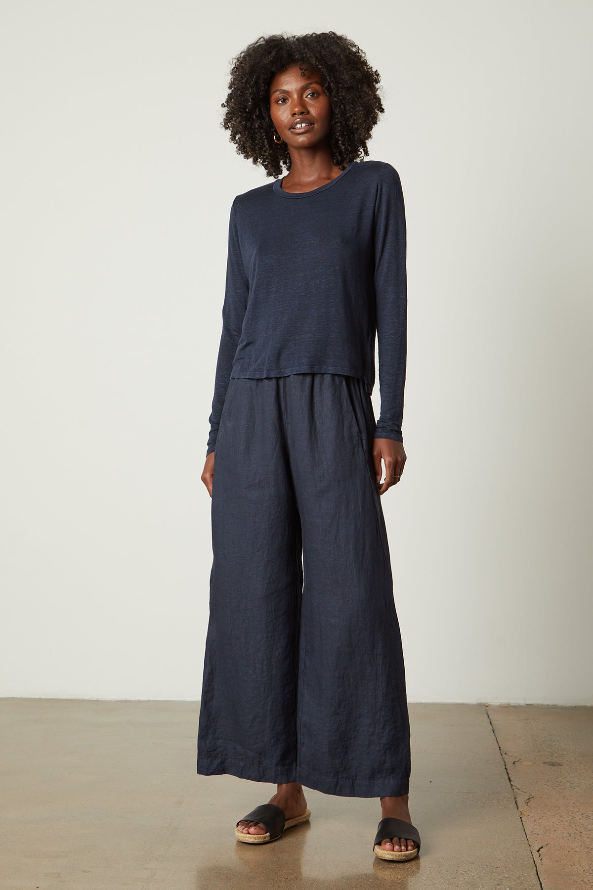   The model is wearing a navy KARA CREW NECK TEE made by Velvet by Graham & Spencer, providing a perfect base layer for the wide leg pants. The ensemble showcases a natural texture. 