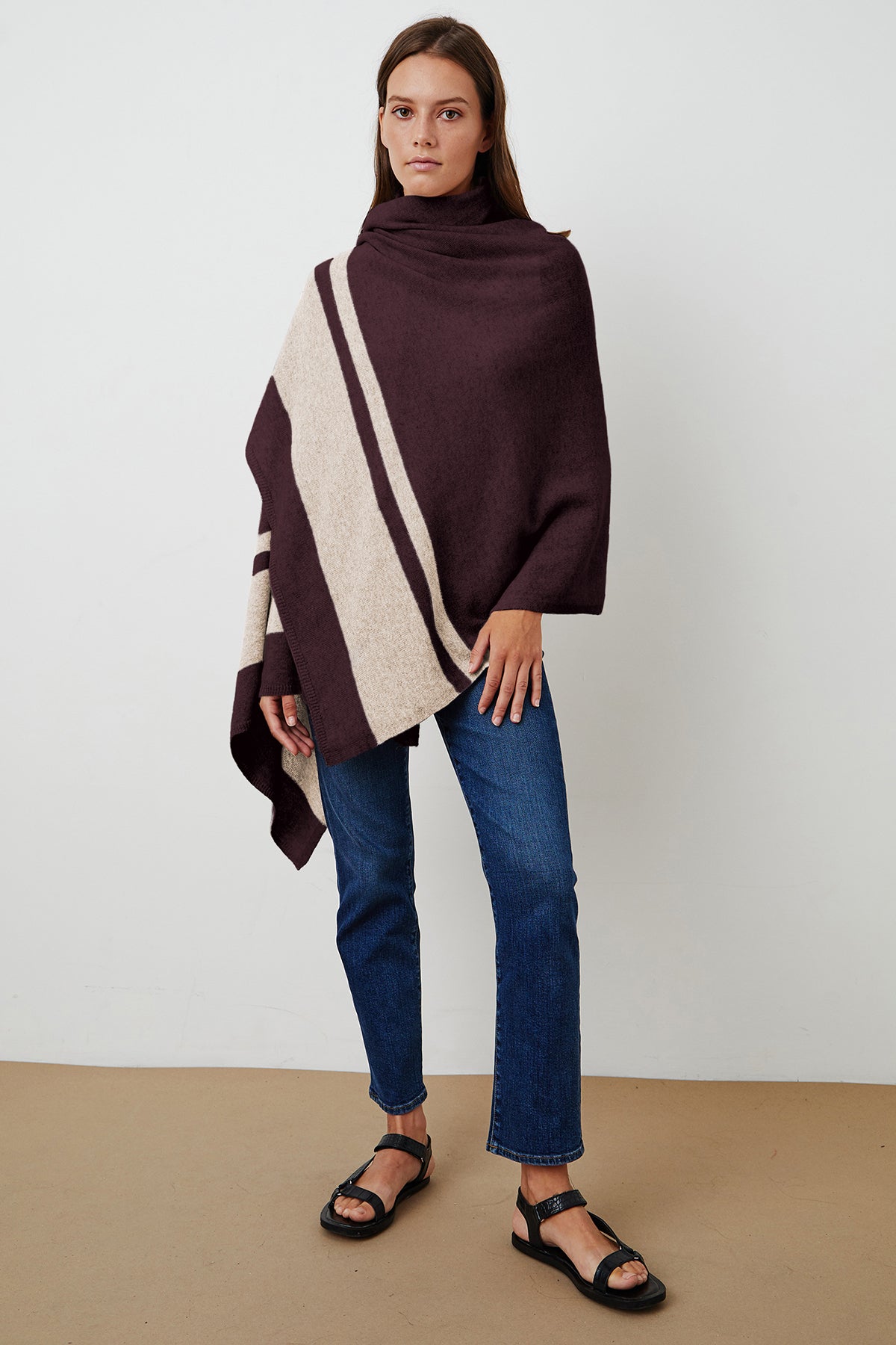   A cozy woman wearing a burgundy and beige striped poncho made of Jenny Graham Home's LIV Cashmere Throw Blanket. 