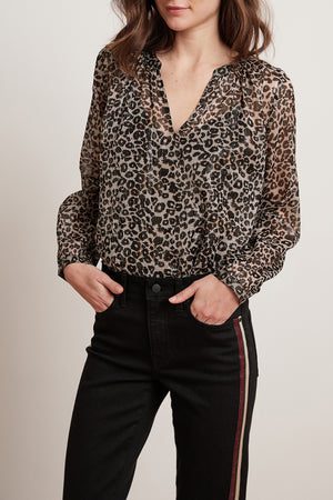 A person wearing the Velvet by Graham & Spencer PEYTON LEOPARD LUREX LONG SLEEVE BLOUSE tucked into high-waisted black pants with side stripes, showcasing perfect day-to-night versatility.