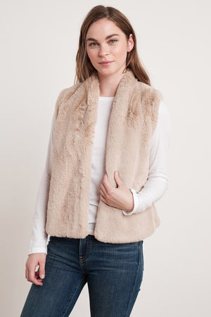 Person with long hair wearing a white top, the CHELLE FAUX LUX FUR OPEN VEST by Velvet by Graham & Spencer, and jeans, standing against a plain background. This stylish layering piece is perfect for the cooler months.