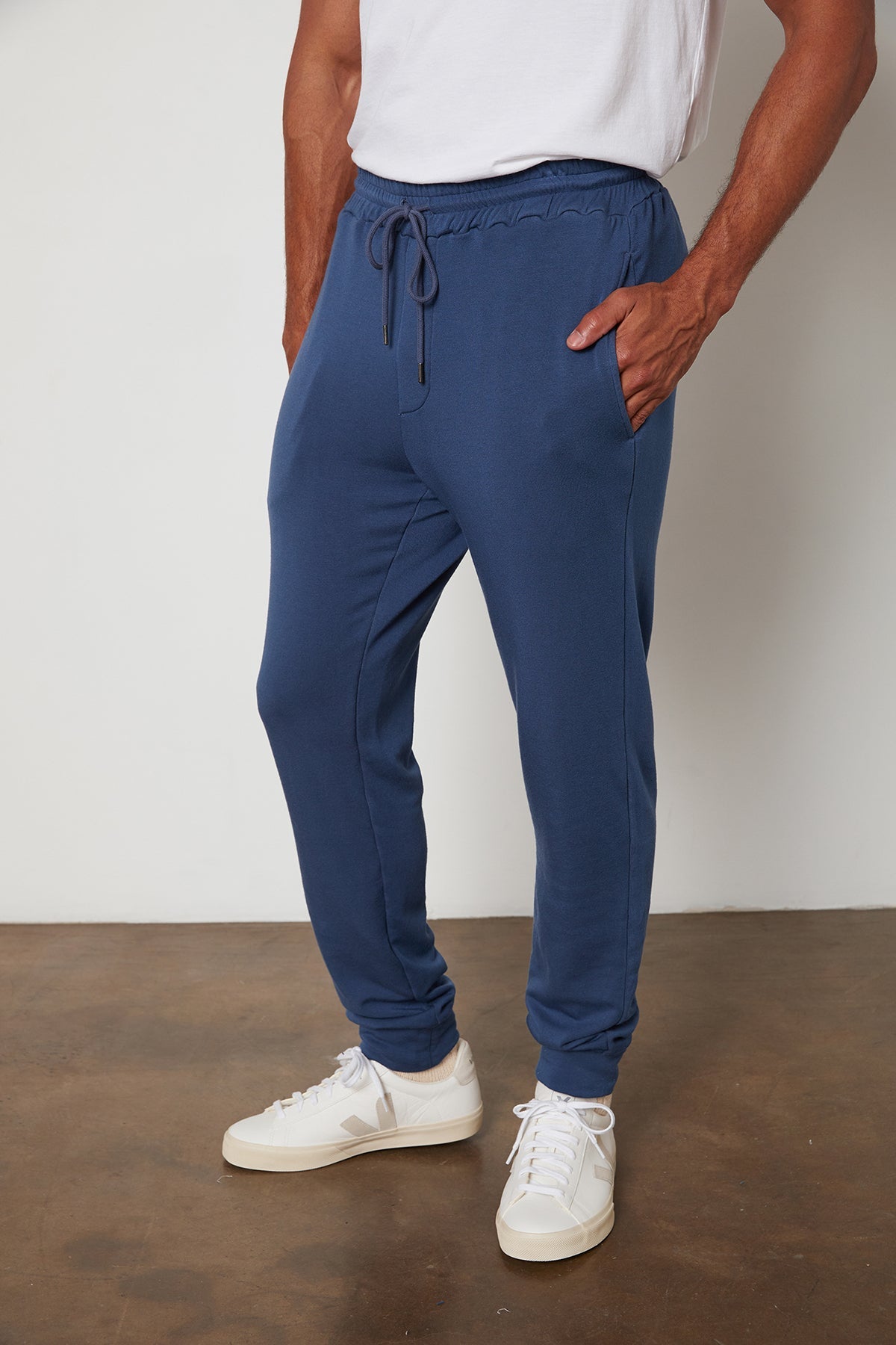 A person is standing against a plain background, wearing a white t-shirt, CROSBY LUXE FLEECE JOGGER by Velvet by Graham & Spencer—ideal for workouts—and white sneakers.-25051977613505