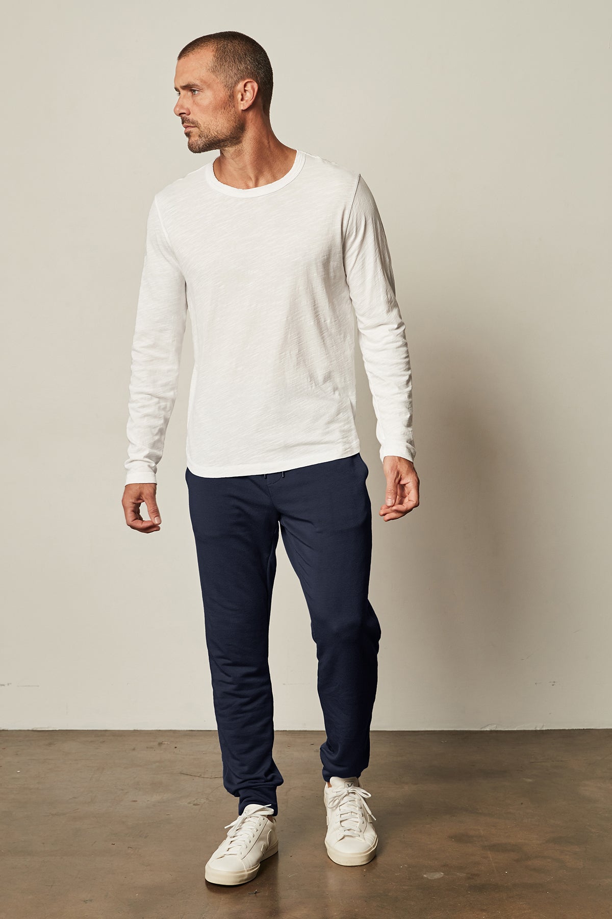   The model is wearing a white t-shirt and navy Velvet by Graham & Spencer CROSBY LUXE FLEECE JOGGER sweatpants. 