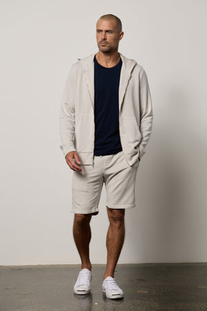 A man, always on heavy rotation, is wearing a Velvet by Graham & Spencer ATLAS LUXE FLEECE DRAWSTRING SHORT hoodie and classic-style shorts in beige.
