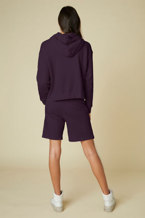 The back view of a woman wearing Velvet by Jenny Graham's LAGUNA SWEATSHORT with an elastic waist, paired with a purple hoodie.