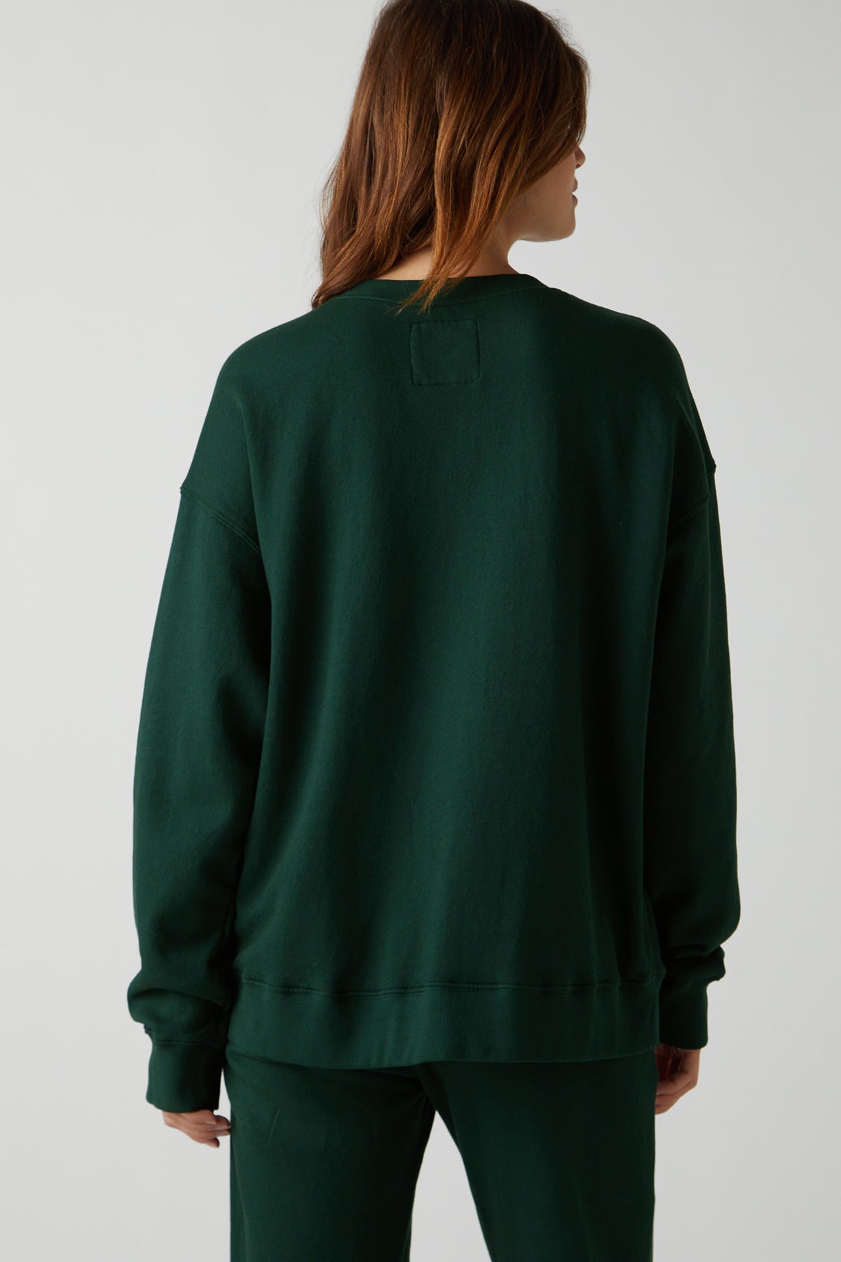  The back view of a woman wearing a green Velvet by Jenny Graham Abbot Sweatshirt, made from organic cotton, showcasing its slouchy and styling versatility. 