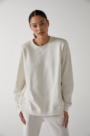The model is wearing a slouchy white Abbot sweatshirt and sweatpants made from organic cotton by Velvet by Jenny Graham.