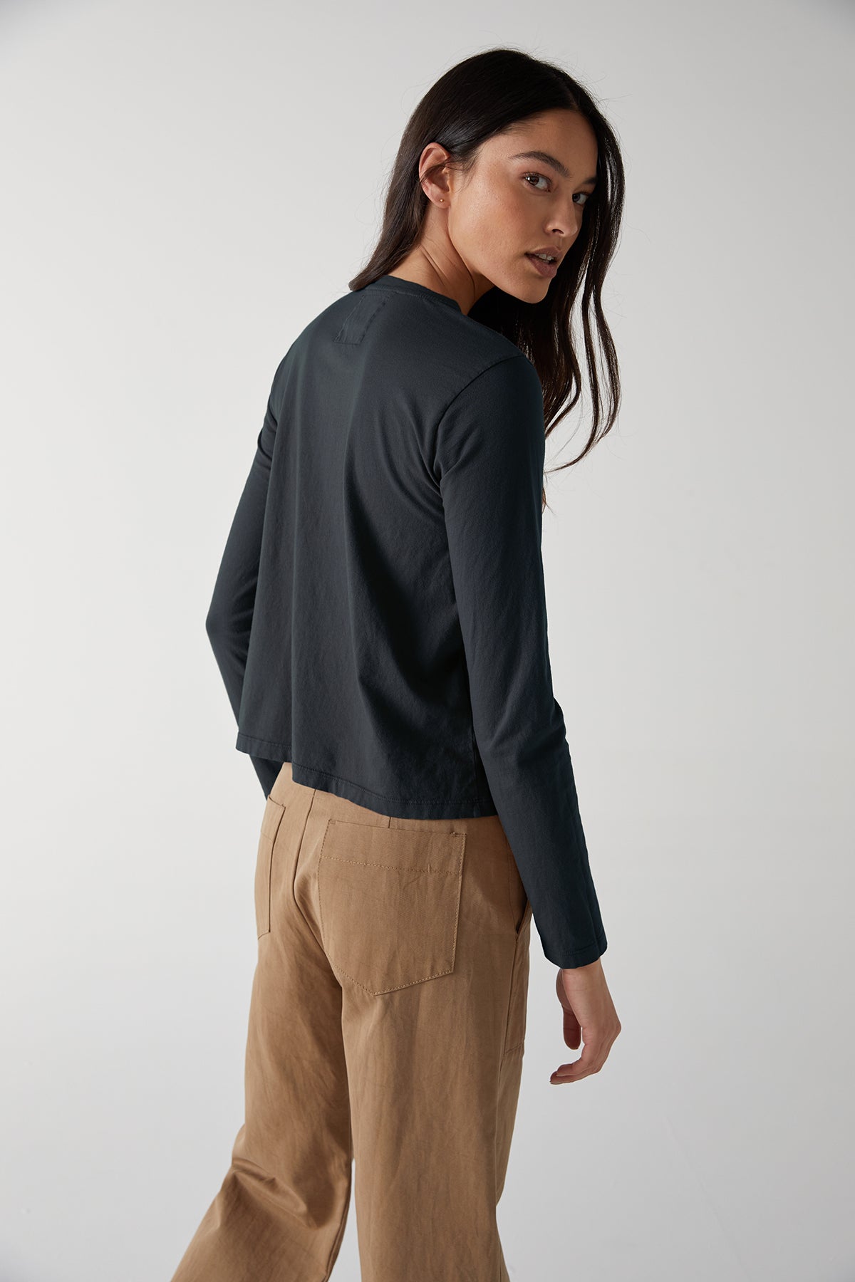 The back view of a woman wearing tan trousers and a black long sleeved VICENTE TEE by Velvet by Jenny Graham.-24427644125377