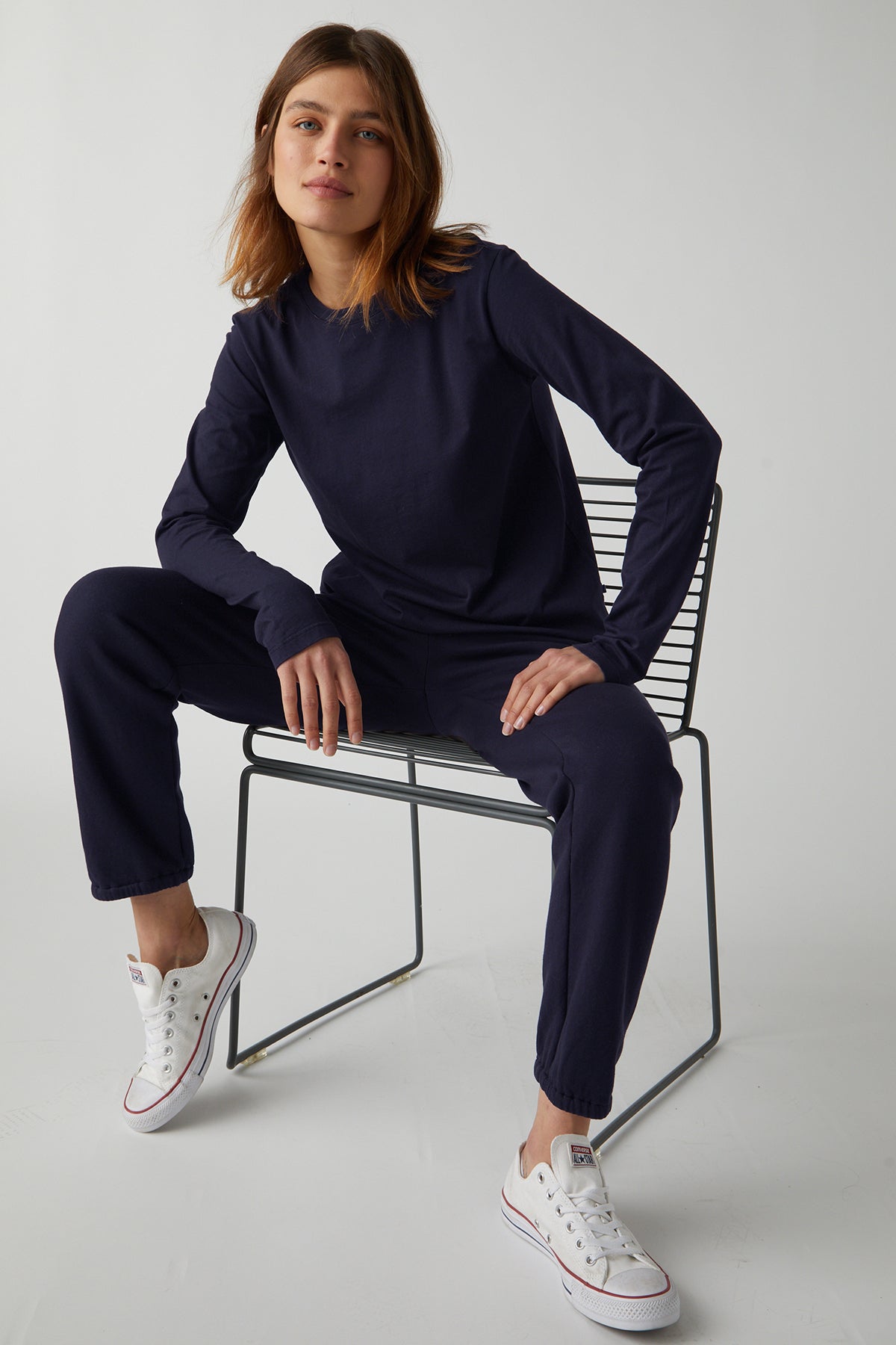 Model sitting in wire chair wearing Vicente Tee in navy with Zuma Sweatpant and Converse full length front-26007106224321