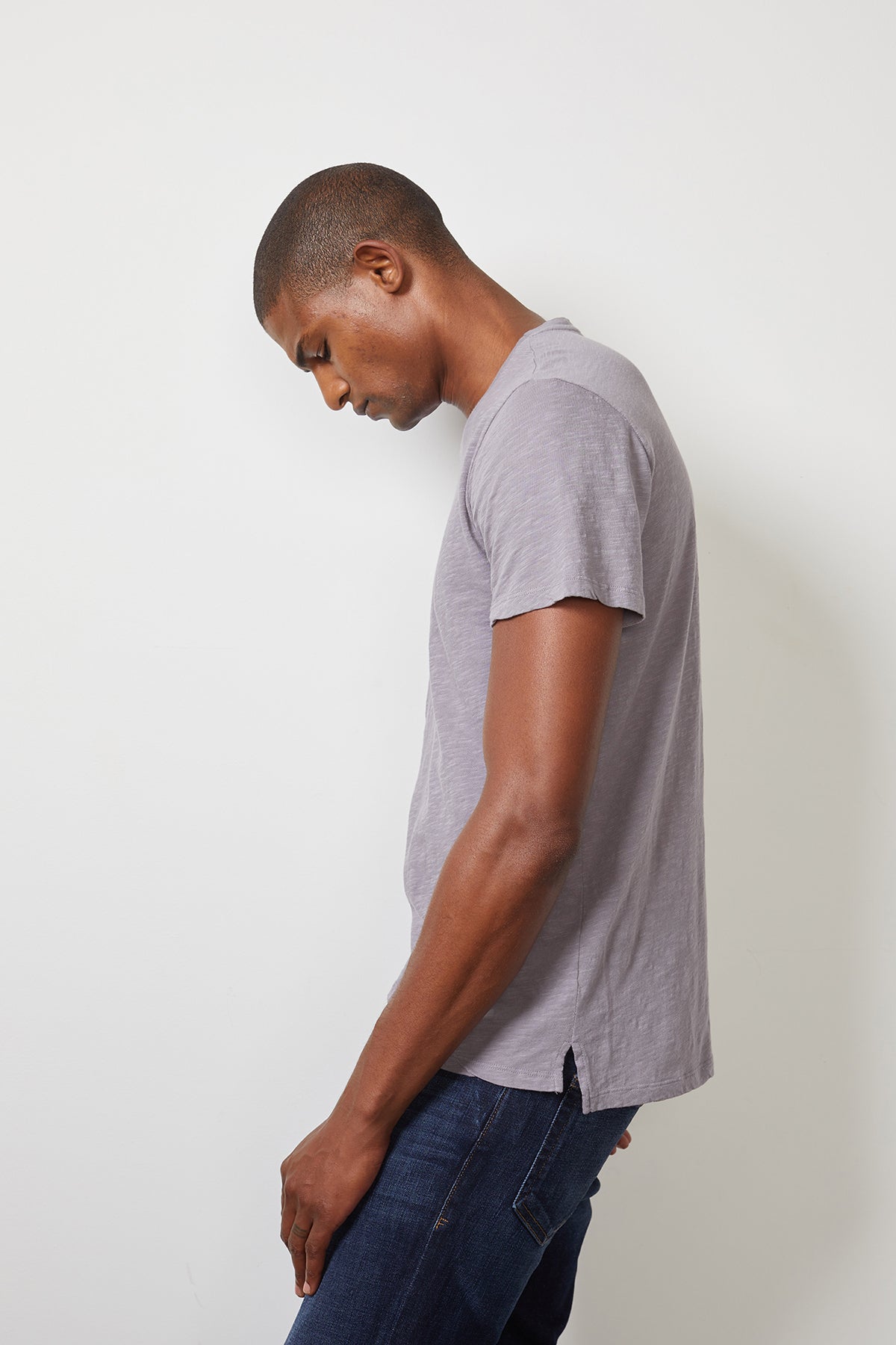 A man in a Velvet by Graham & Spencer Dion Crew Neck Tee and jeans is leaning against a wall.-22095008170177