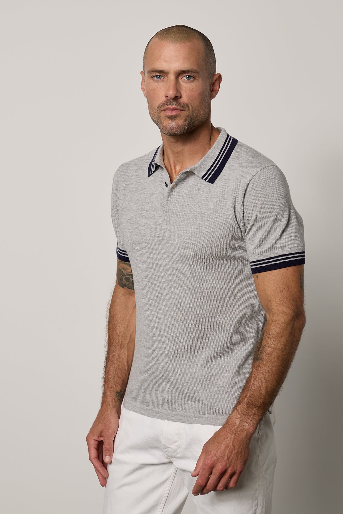 A man wearing a Velvet by Graham & Spencer FINLEY PIQUE POLO, featuring a textured fine ribbing and classic design, is seen in white pants.-26184040251585