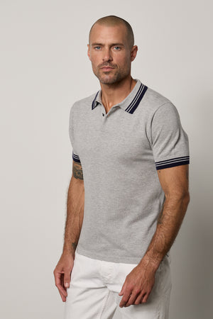 A man wearing a Velvet by Graham & Spencer FINLEY PIQUE POLO, featuring a textured fine ribbing and classic design, is seen in white pants.
