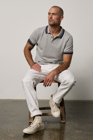 A man, wearing a Velvet by Graham & Spencer FINLEY PIQUE POLO shirt, is sitting on a stool.