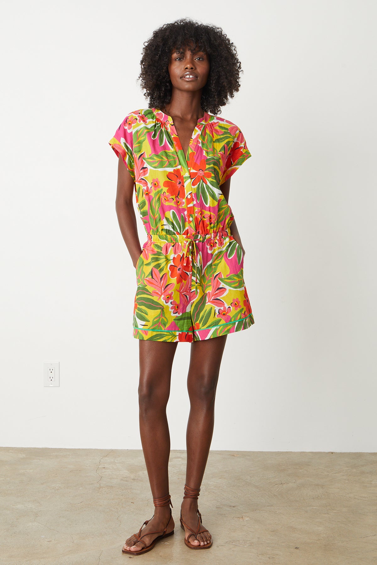   Pam Romper in bold floral aloha print with reds, hot pinks and greens full length front models hands in both pockets 