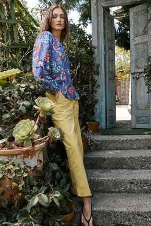 Model standing on garden steps outdoors wearing Camryn Top in colorful spring floral print with Mya pant in yellow aurora color side & front