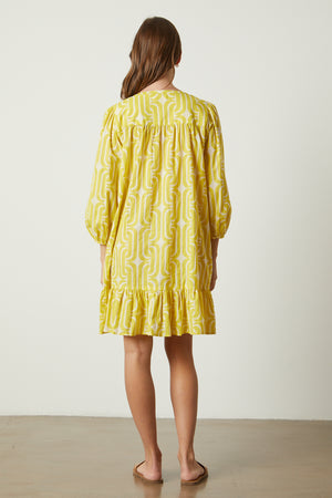 The back view of a woman wearing a Velvet by Graham & Spencer FELICITY PRINTED BOHO DRESS with a ruffled hemline.