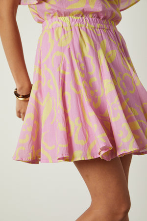 A woman in a pink and yellow dress posing in the ELSA PRINTED SKIRT by Velvet by Graham & Spencer.