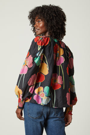 Avery Top in bold floral with black background and blue denim back model looking over shoulder