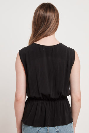 A woman in a black peplum top with a cinched waist and cross-over front, the ADALI WRAP BLOUSE by Velvet by Graham & Spencer.