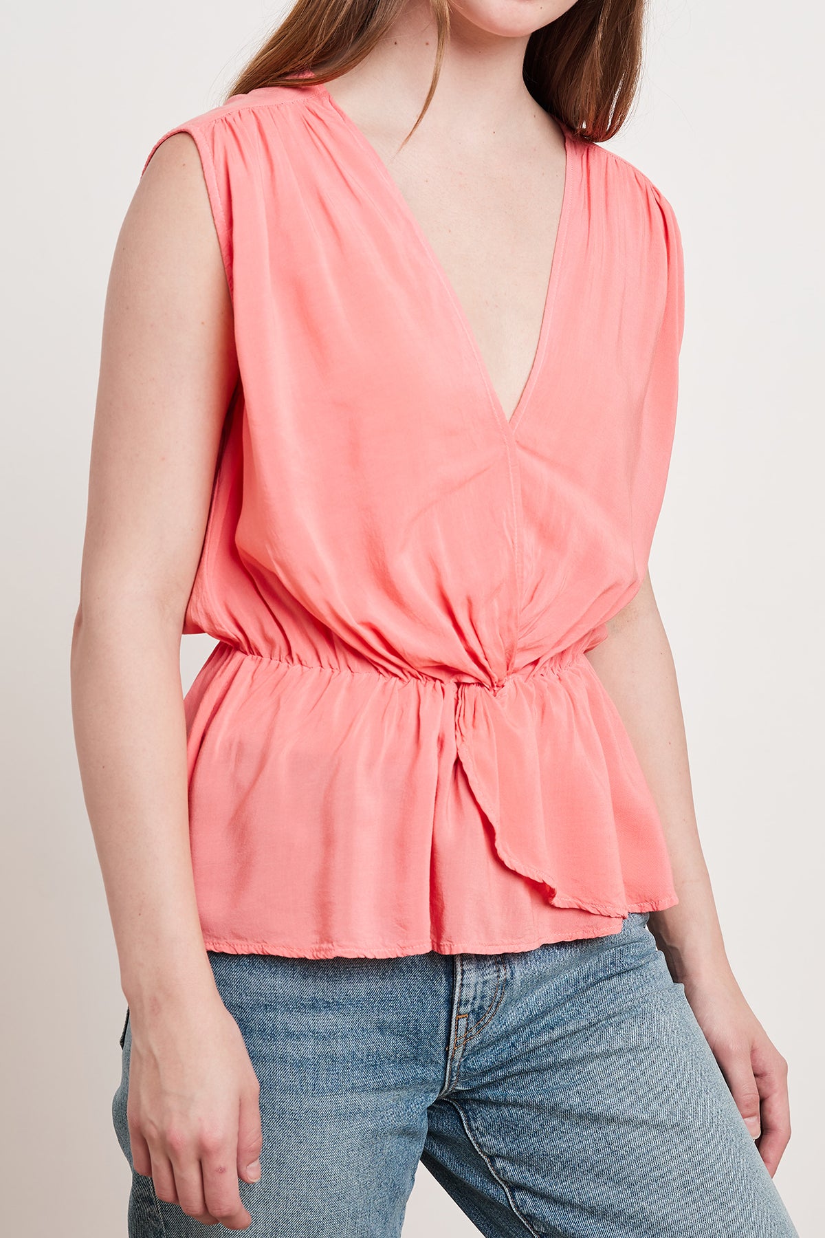 A woman wearing a Coral ADALI WRAP BLOUSE top and jeans with a cinched waist.-24193744699585