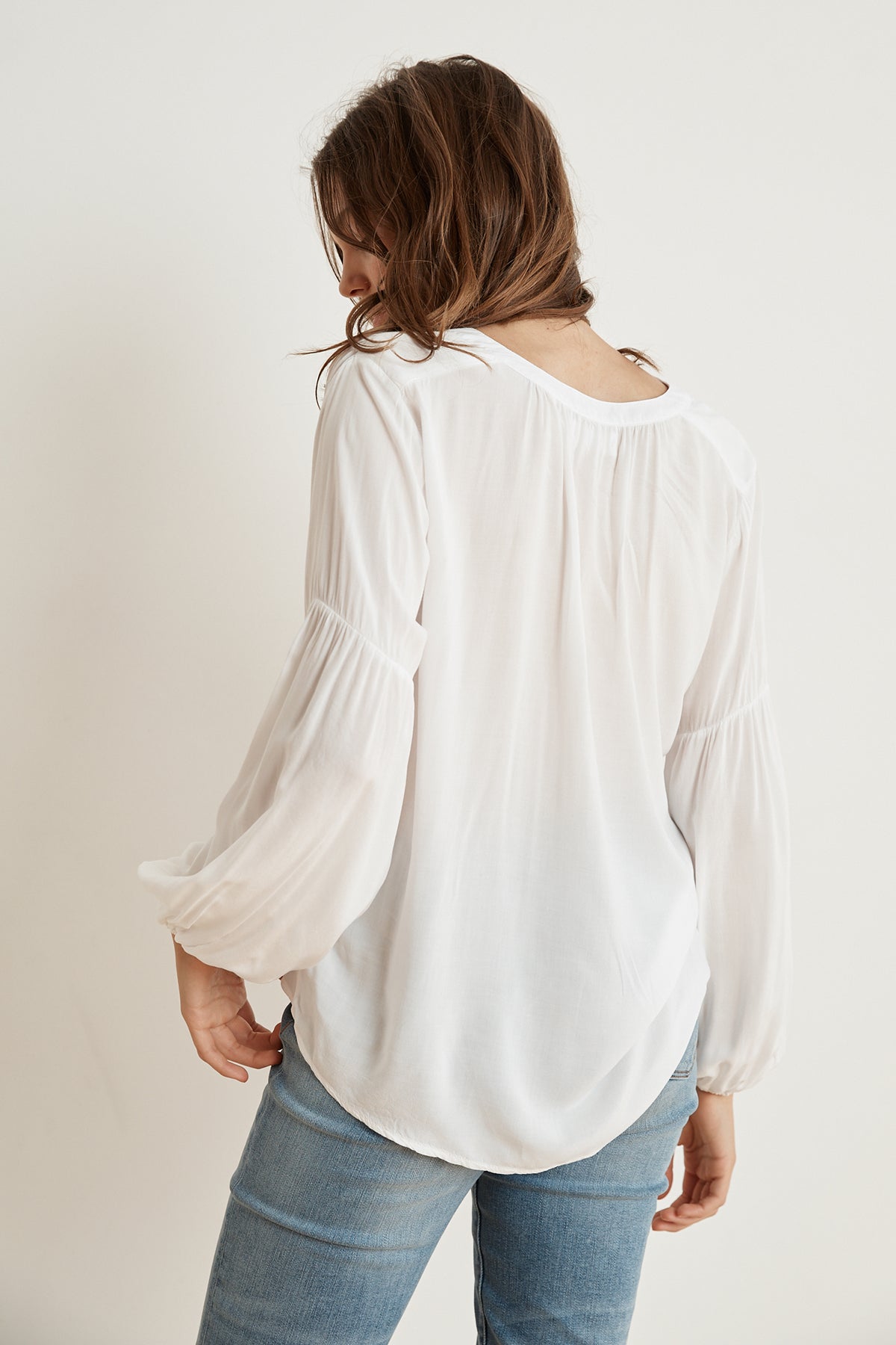   The back view of a woman wearing jeans and a Yulia Rayon Challis Peasant Sleeve Blouse by Velvet by Graham & Spencer, giving off a breath of fresh air. 