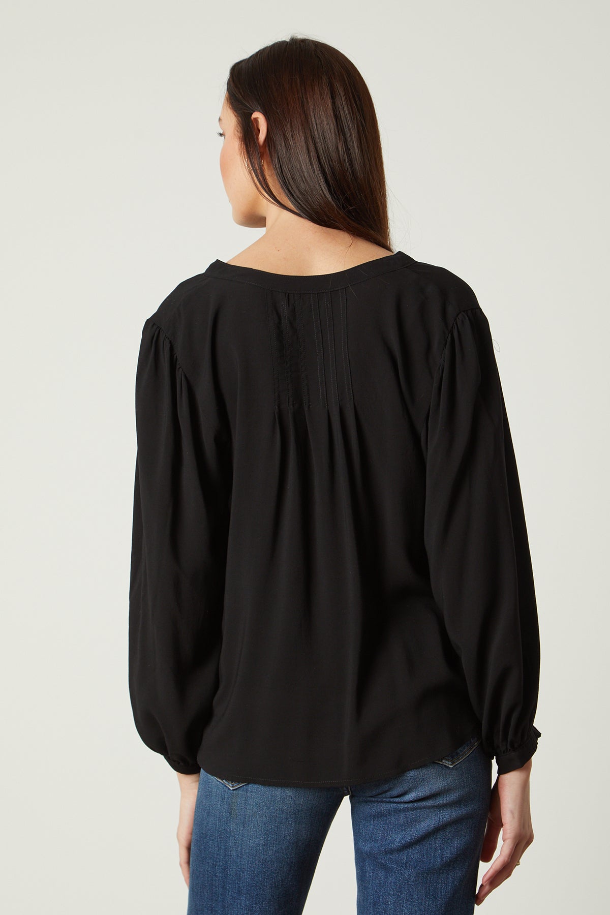 the back view of a woman wearing jeans and an EMILY V-NECK BLOUSE by Velvet by Graham & Spencer.-25954485731521
