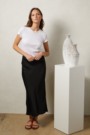 a woman wearing a white t-shirt and the Velvet by Graham & Spencer AUBREE SATIN MIDI SKIRT.