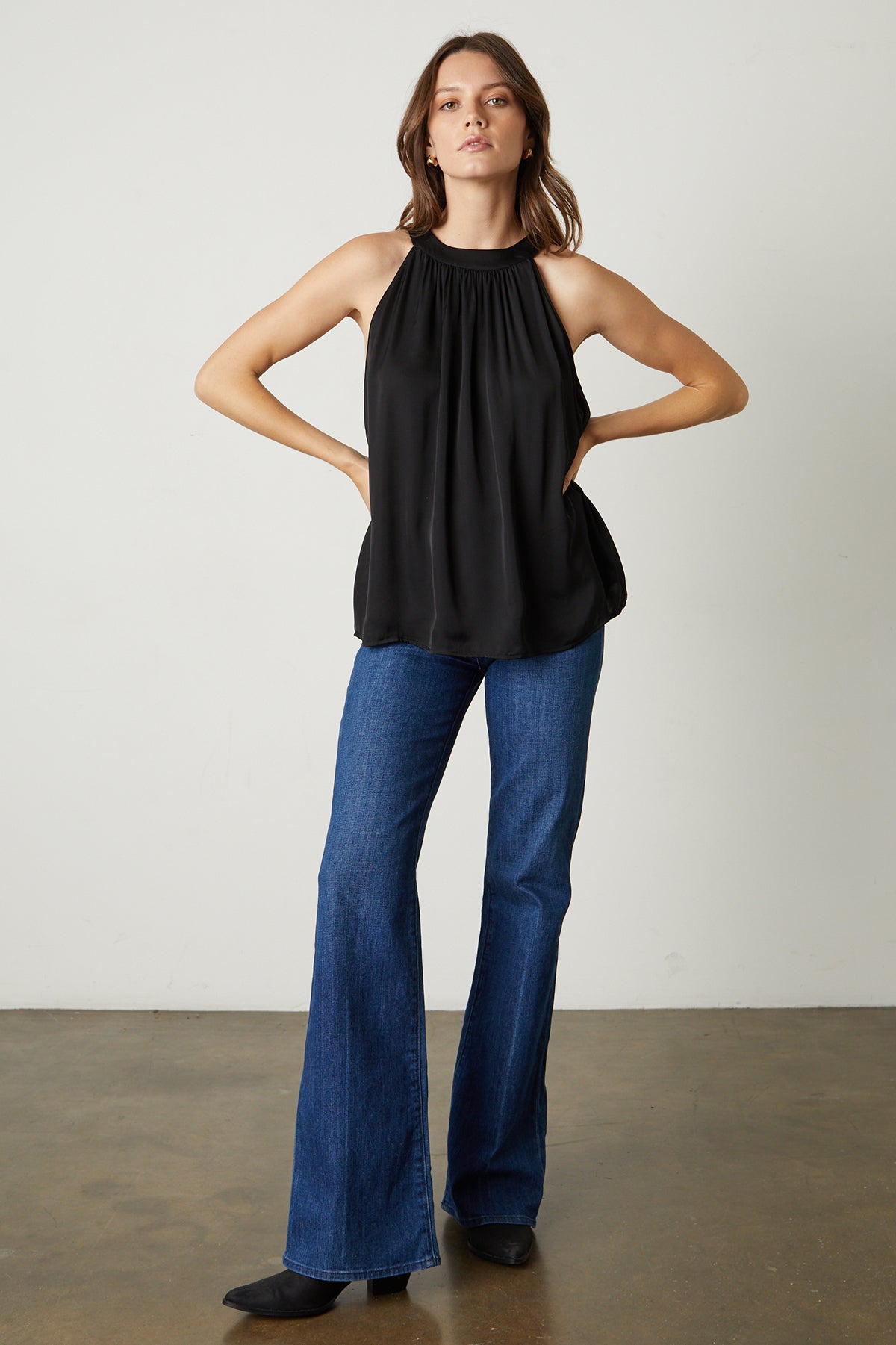Model standing with hands on hips wearing Crystal Satin Halter Top in black with blue denim and black boots full length front-25548656705729