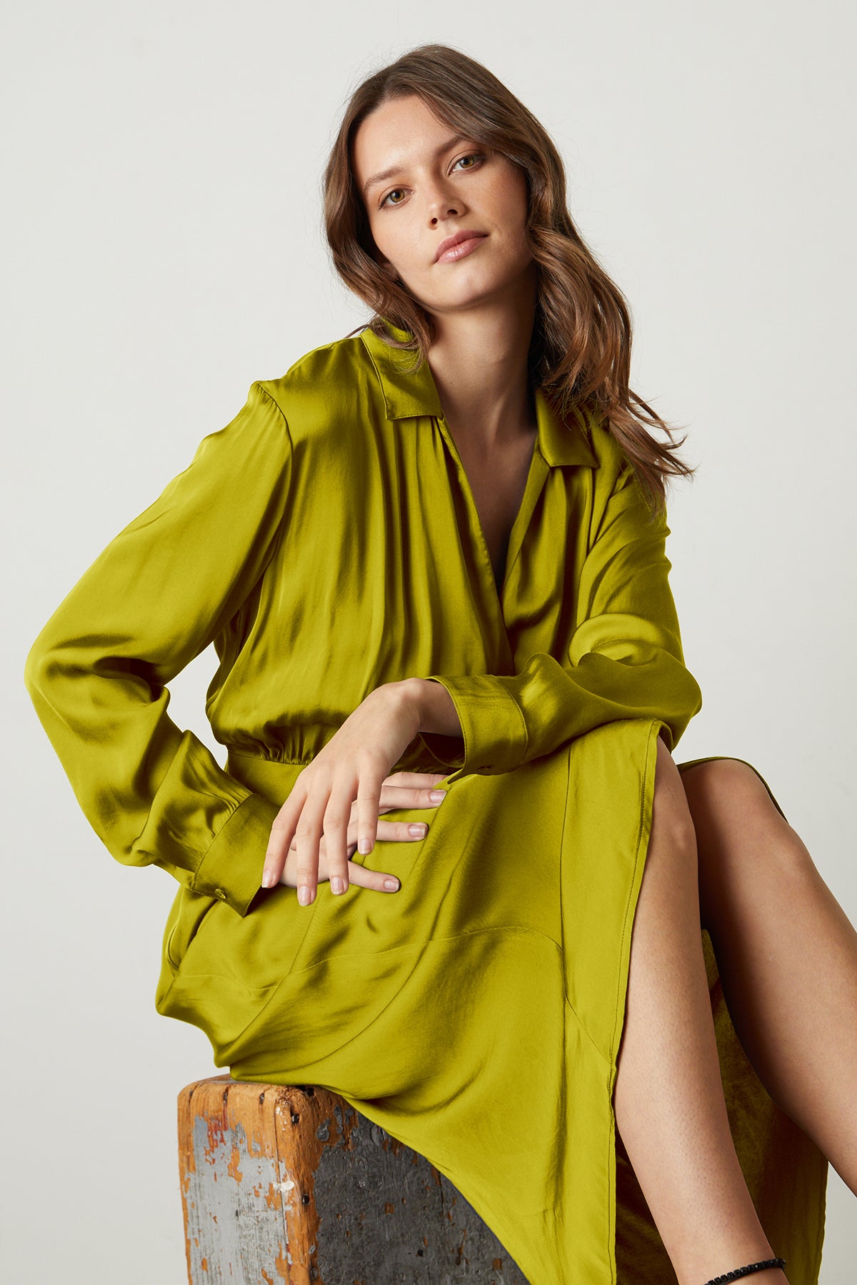 Model sitting on stool wearing Jovie Satin Wrap Dress in bright meadow green front-25994845126849