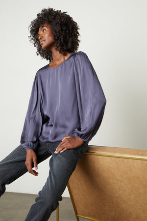A woman is sitting on a bench in a Velvet by Graham & Spencer LEILA SATIN PUFF SLEEVE BLOUSE.