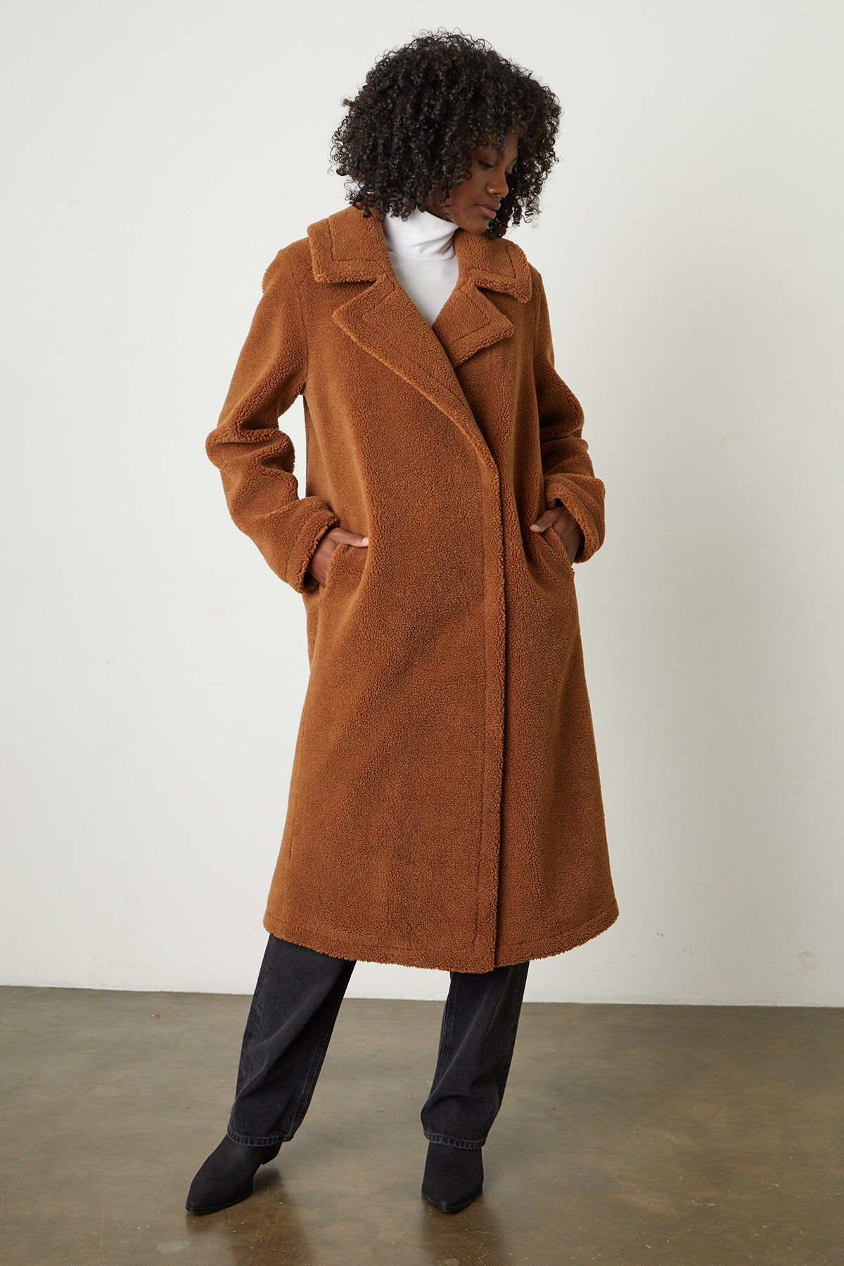   A woman wearing a REINA FAUX SHEARLING COAT by Velvet by Graham & Spencer with double-breasted silhouette and popper button closures. 