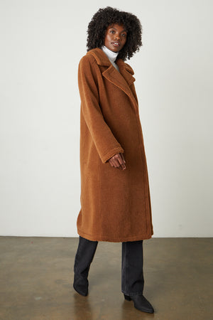 The model is wearing a REINA FAUX SHEARLING COAT by Velvet by Graham & Spencer with a double-breasted silhouette and faux shearling collar.